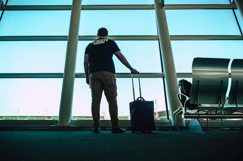 Reisetipps für deine Reiseplanung man with luggage waiting at airport lounge anticipating departure in a modern setting. 1381415 Mann wartet mit Gepäck am Fenster.