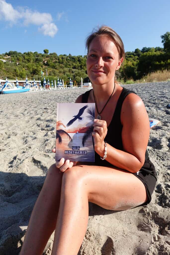 Fiat Ducato als Camper - Warum wir uns für den L5H2 entschieden haben reisetagebuch italien 1 Frau am Strand hält Buch "Mein Reise Tagebuch" mit Vogelmotiv, Sonne und Wasser im Hintergrund.