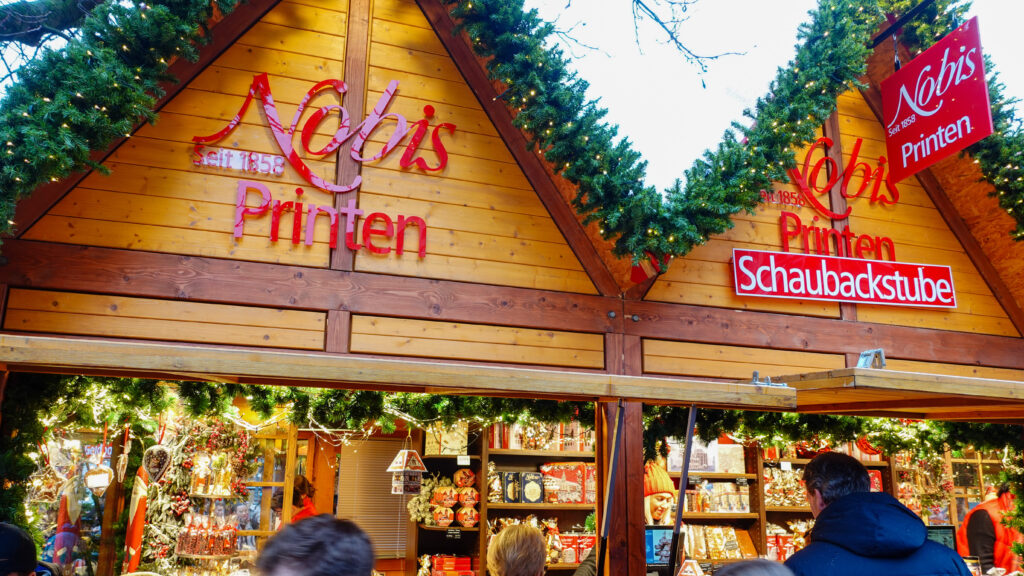 Detailaufnahme eines Printen- und Gebäckstandes auf dem Weihnachtsmarkt in Aachen mit beleuchteten Holzbuden.