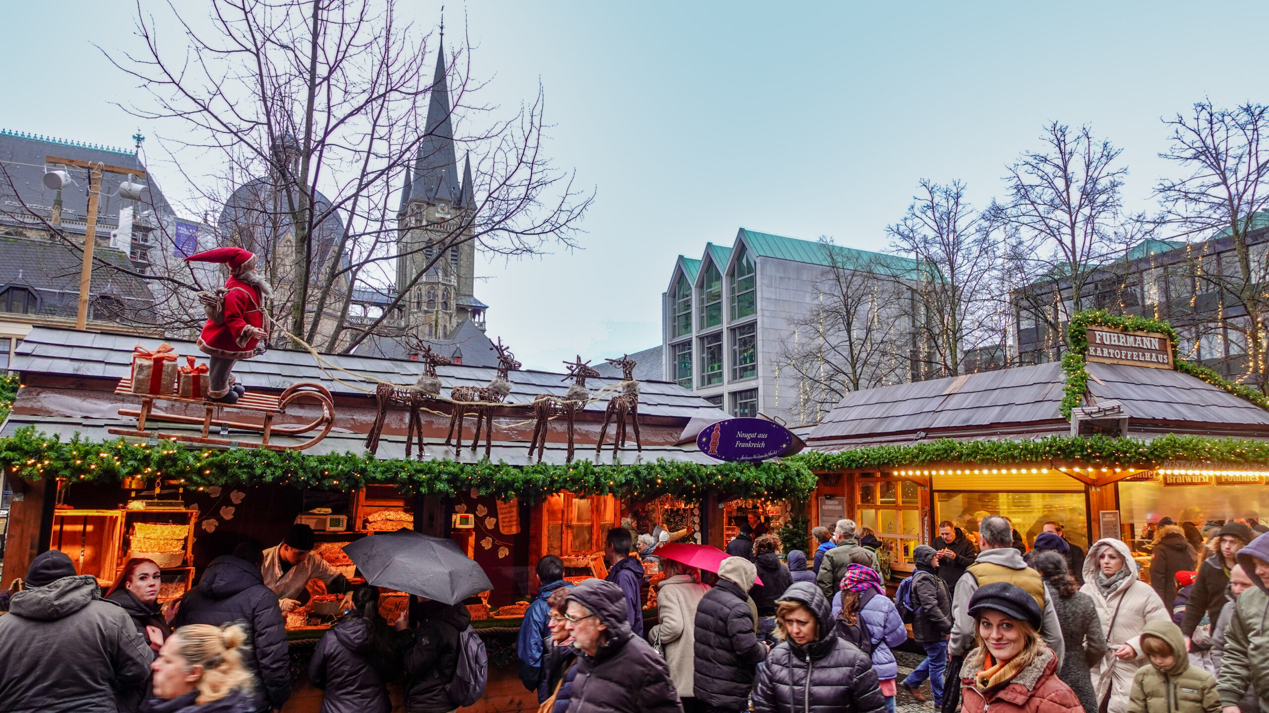 Aachener Weihnachtsmarkt bei Dämmerung mit festlich beleuchteten Ständen und Menschen, die durch die Gassen schlendern.
