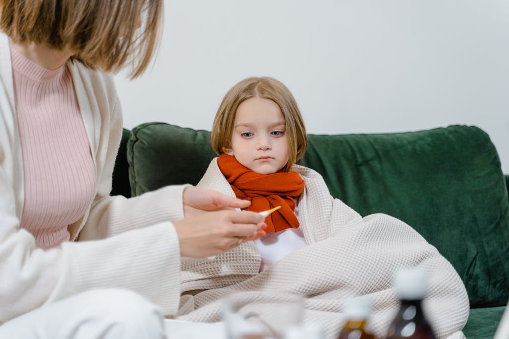 Reiseversicherung für Familien: Welche brauchst du wirklich? Unsere ehrliche Empfehlung a caring moment of a woman checking a sick childs temperature on a cozy green couch indoors. 8376203 A caring moment of a woman checking a sick child's temperature on a cozy green couch indoors.