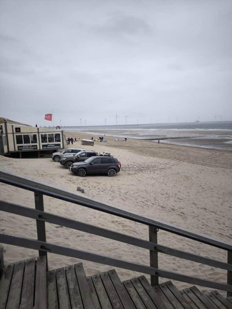 Camping in Burgh-Haamstede: Unsere Tipps für den Familienurlaub in den Niederlanden strand bei burhaam stede Strand mit Parkplätzen, Windkraftanlagen und bewölktem Himmel.