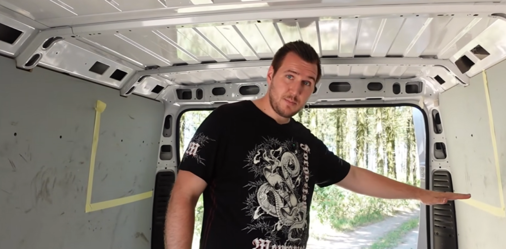Mann zeigt auf den Innenraum eines Vans Camper-Ausbau Fiat Ducato und plant den Grundriss