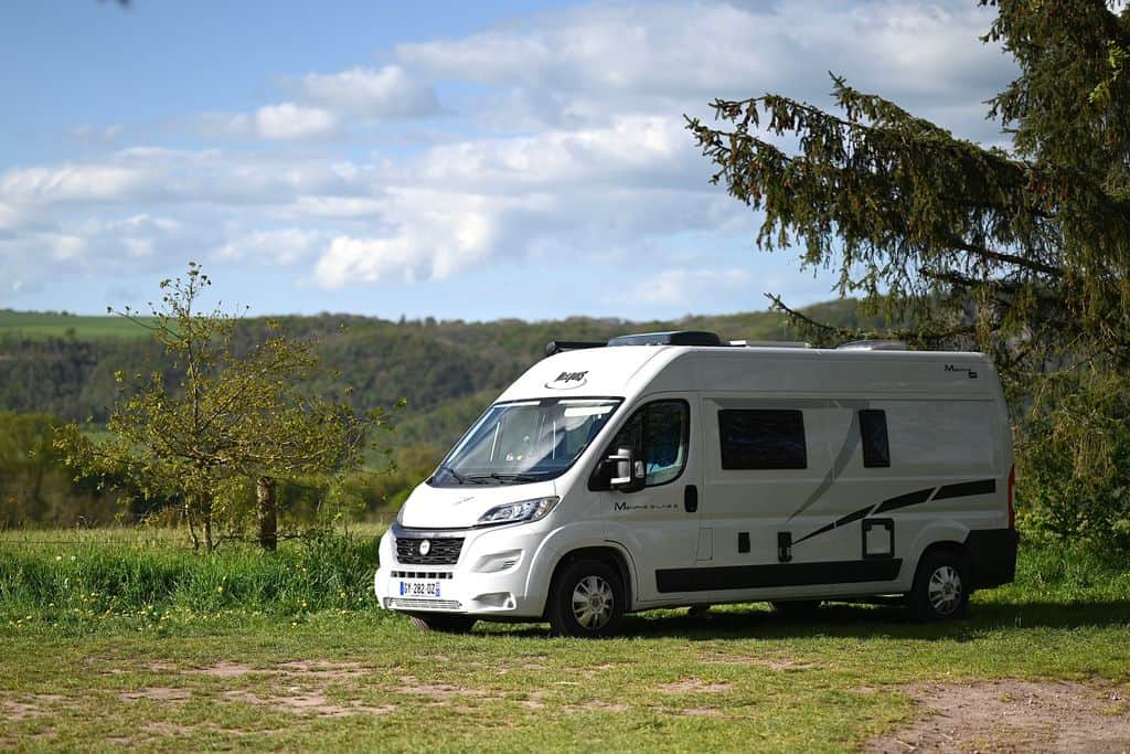 Wohnmobil, Kastenwagen oder Dachzelt – Welches Basisfahrzeug für den Camper-Ausbau? a white camper van sits on a grassy field surrounded by trees under a blue sky. 32378665 campervergleich wohnmobikl