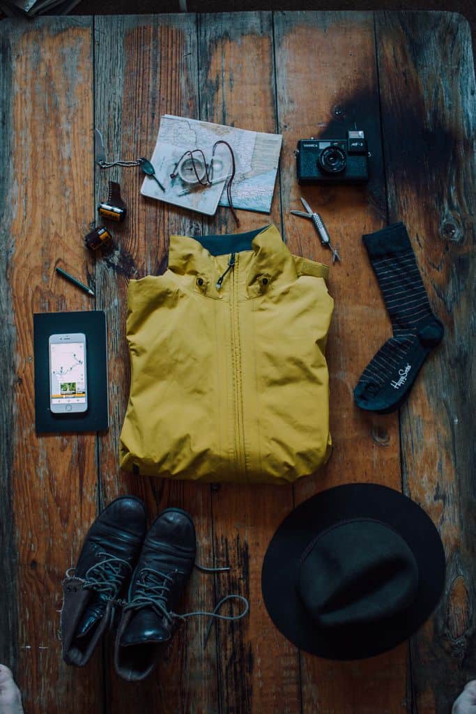 Welche Reiseversicherung brauche ich wirklich? Unser ehrlicher Überblick flat lay of travel gear including jacket shoes camera hat and map on rustic wooden table. 5531402 Packlisten für den Urlaub – unsere wichtigsten Checklisten
