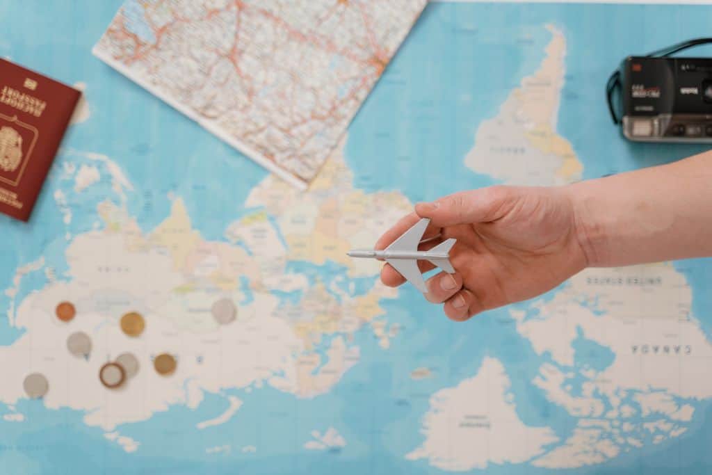 Welche Reiseversicherung brauche ich wirklich? Unser ehrlicher Überblick hand holding a toy airplane over a world map surrounded by coins camera and passport. 7010194 Reiseversicherung beim Campingurlaub: Was Familien wirklich brauchen
